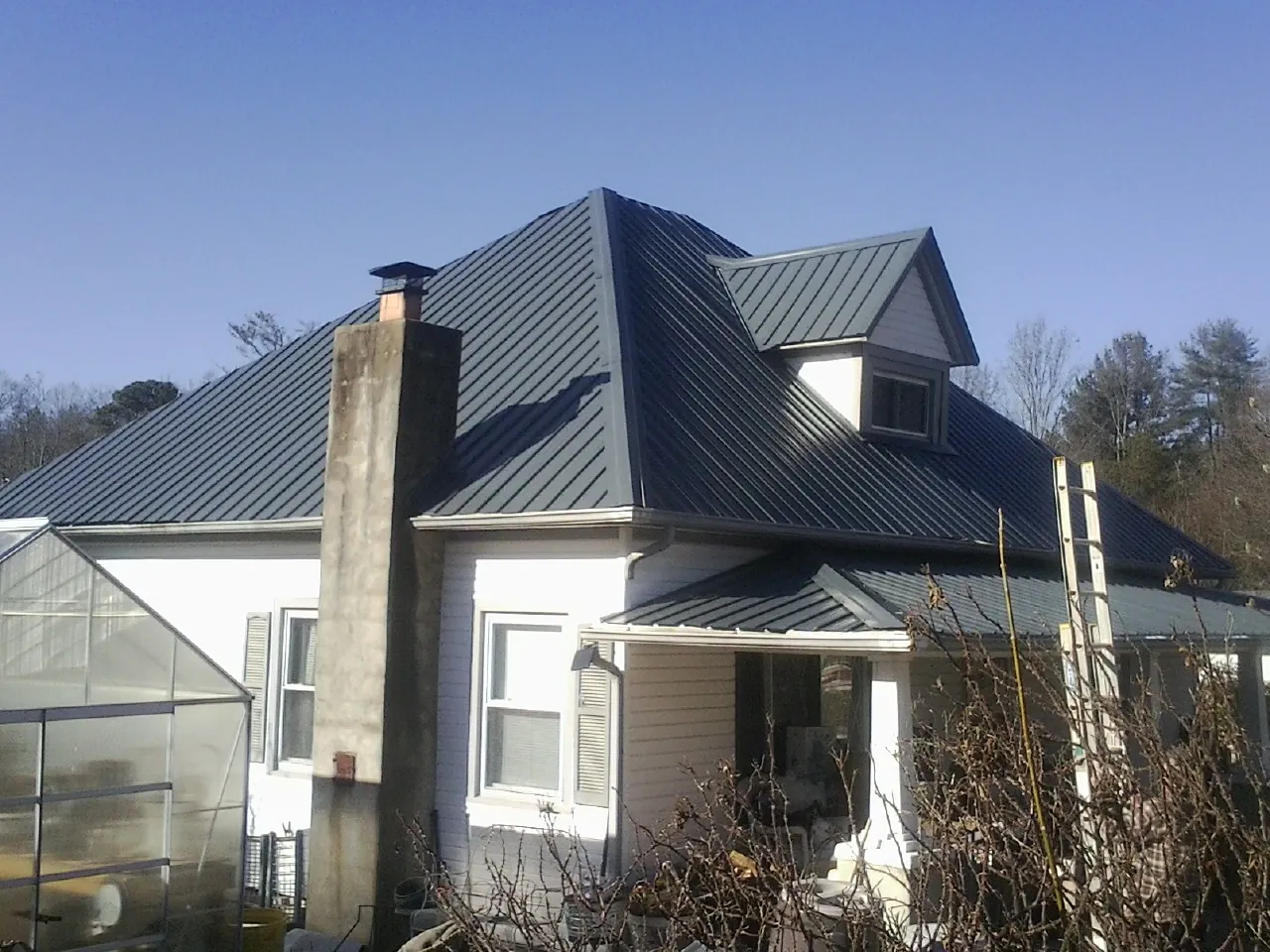 Dark blue standing seam metal roof on a white farmhouse with dormer — Slate & Tile Roof Repair by Roofing Brothers in Mount Kisco