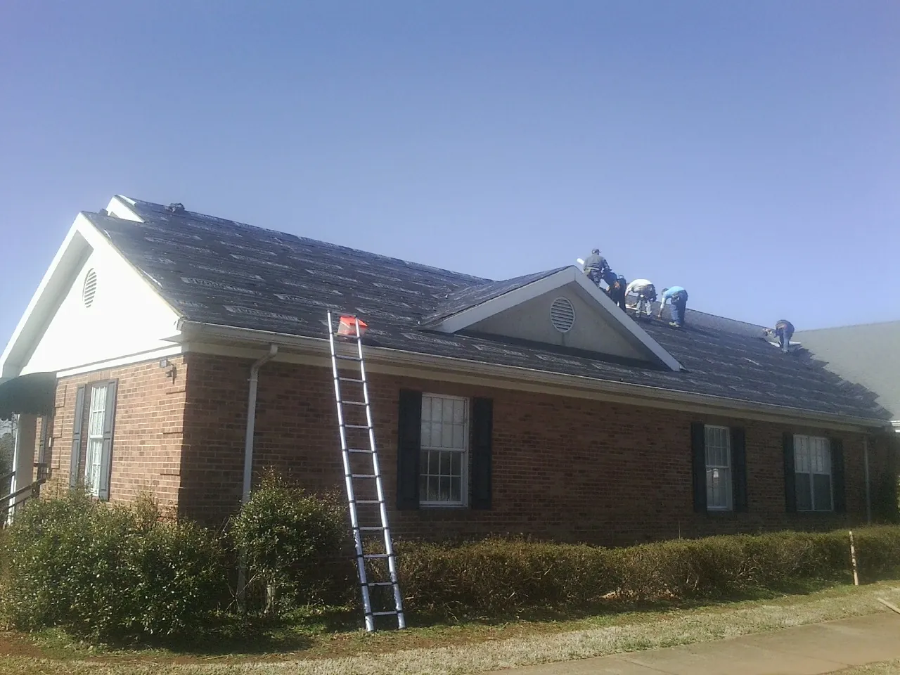 Crew tearing shingles off a brick ranch roof with a ladder set — Emergency Roof Repair work by our crew in Mount Kisco