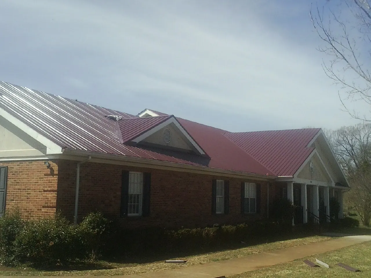 Red metal roof with gabled entries on a long brick building, from a Hail Damage Roof Repair job in Mount Kisco