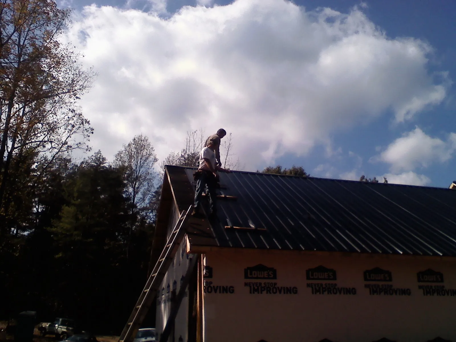 Roofer fastening dark metal panels high against a cloudy sky, from a Roof Inspection job in Mount Kisco