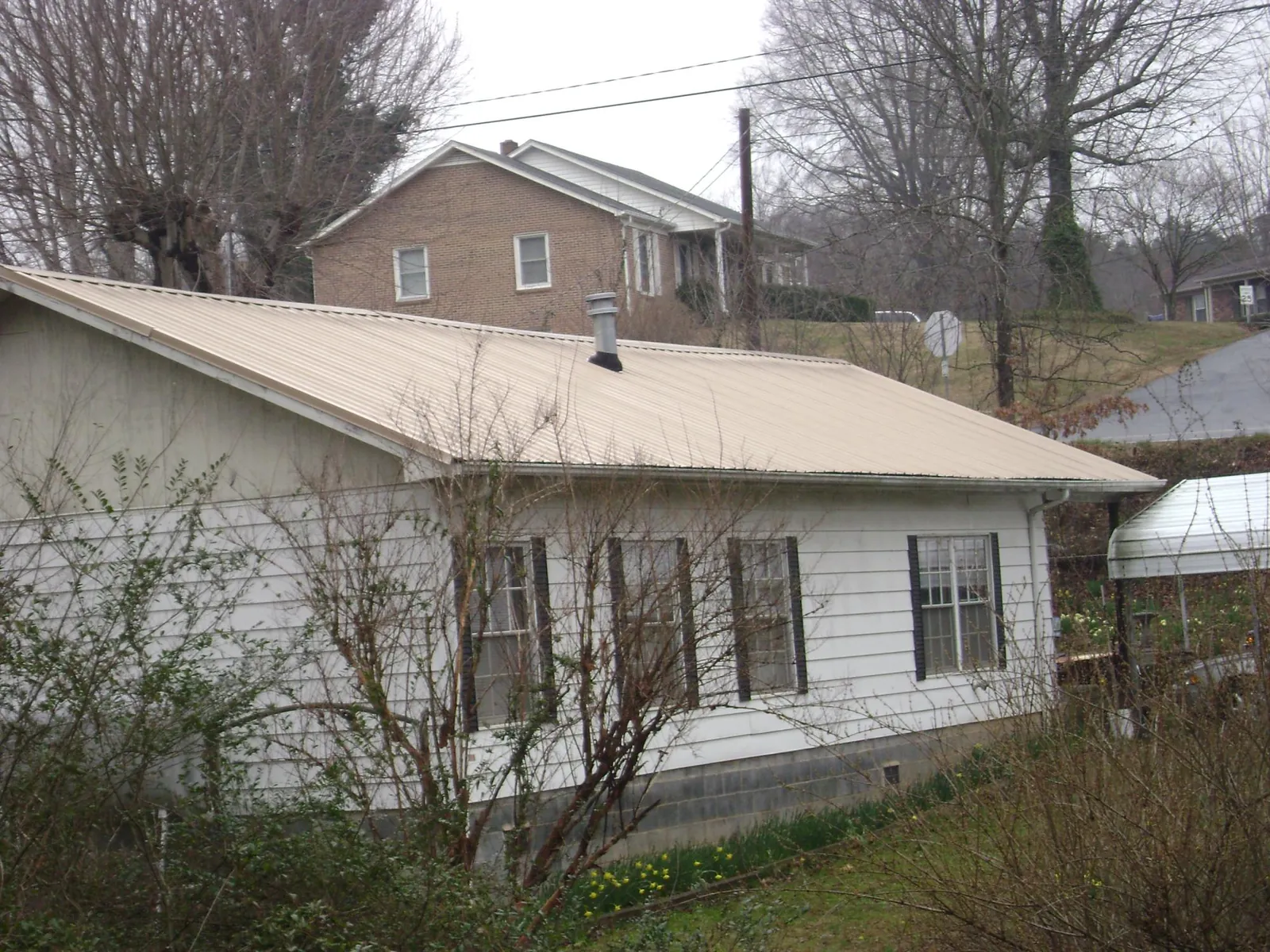 Tan metal roof on a white sided house set into a hillside — Commercial Roofing by Roofing Brothers in Mount Kisco